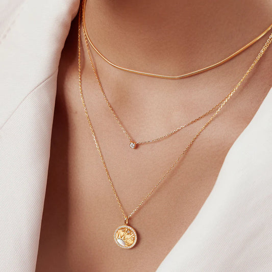 Close-up of a person wearing two gold necklaces with pendants on a neutral background