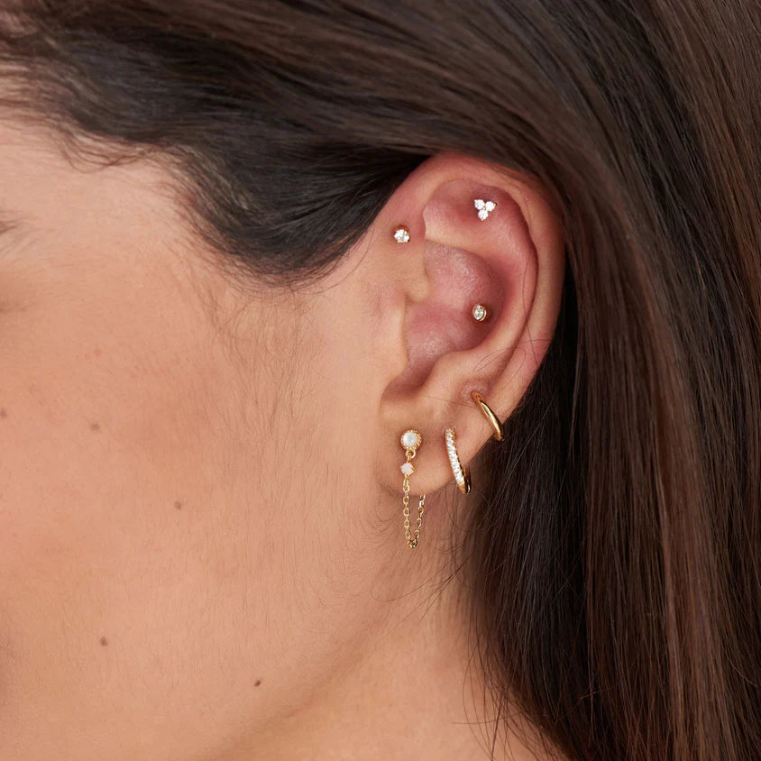 Close-up of an ear with gold hoop earrings and pearl studs.