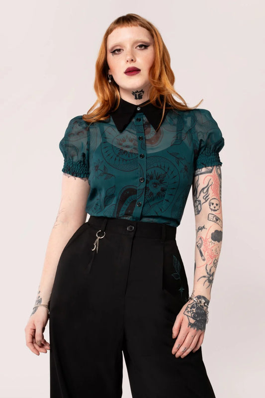 Person wearing a teal blouse with black collar and black pants on a light pink background