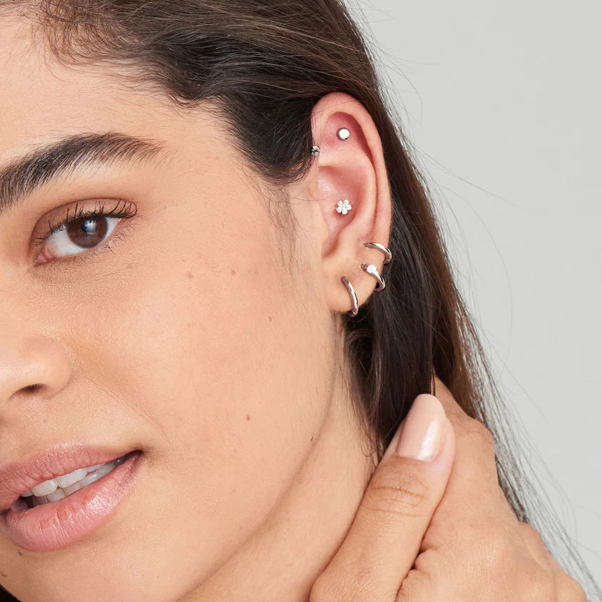 Close-up of a woman's ear with multiple earrings against a neutral background