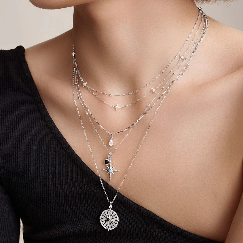 Layered silver necklaces with pendants on a person wearing a black top.